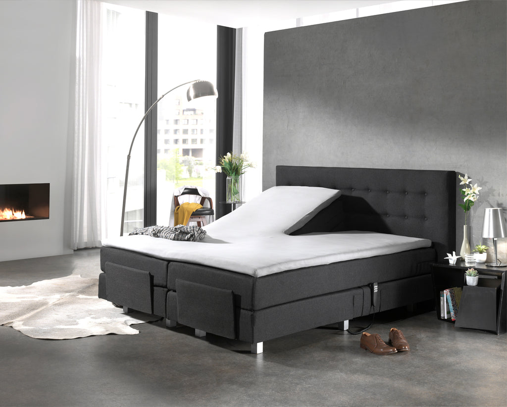 Wit topperlaken op een donkergrijze verstelbare boxspring met één opgeklapt hoofdeinde in een moderne slaapkamer