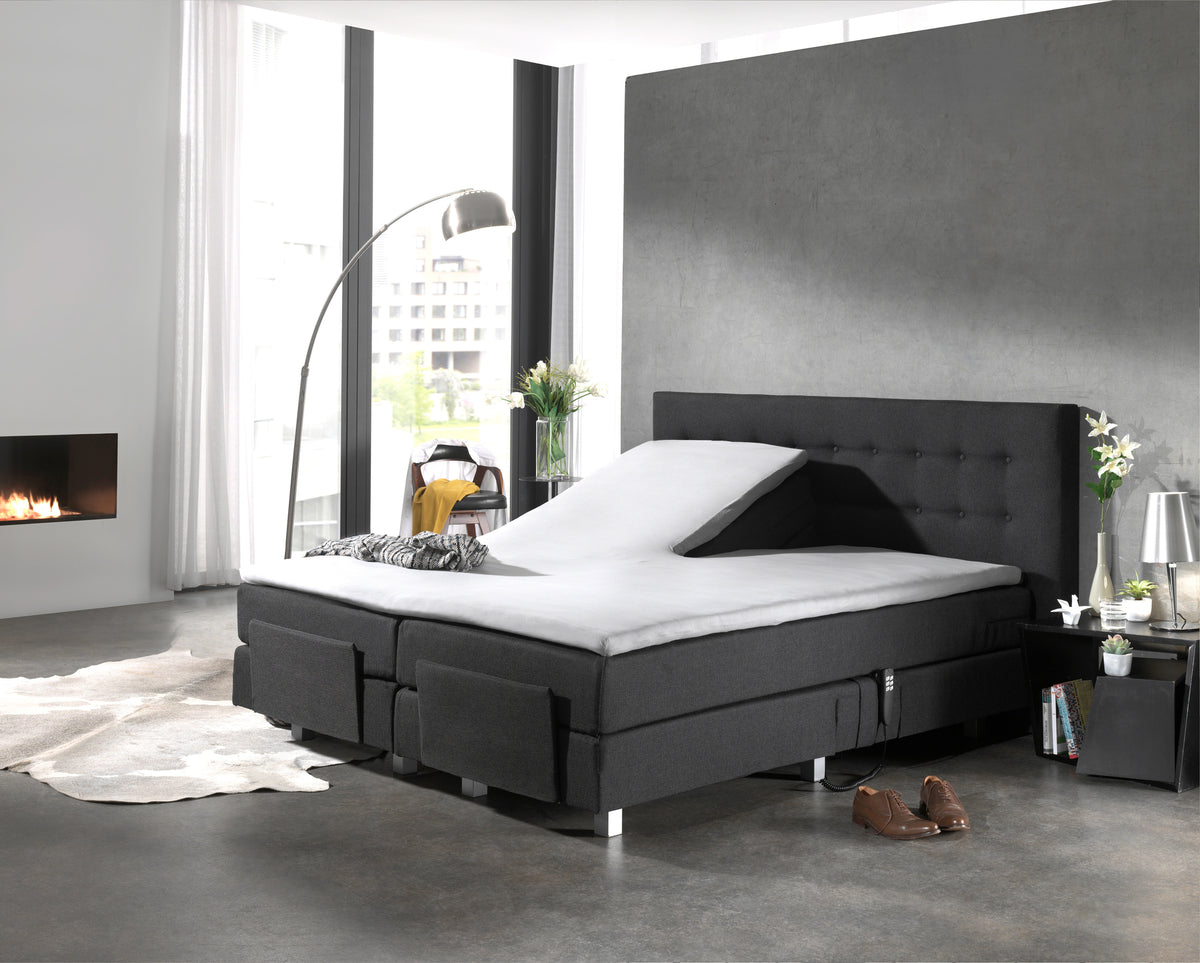 Wit topperlaken op een donkergrijze verstelbare boxspring met één opgeklapt hoofdeinde in een moderne slaapkamer