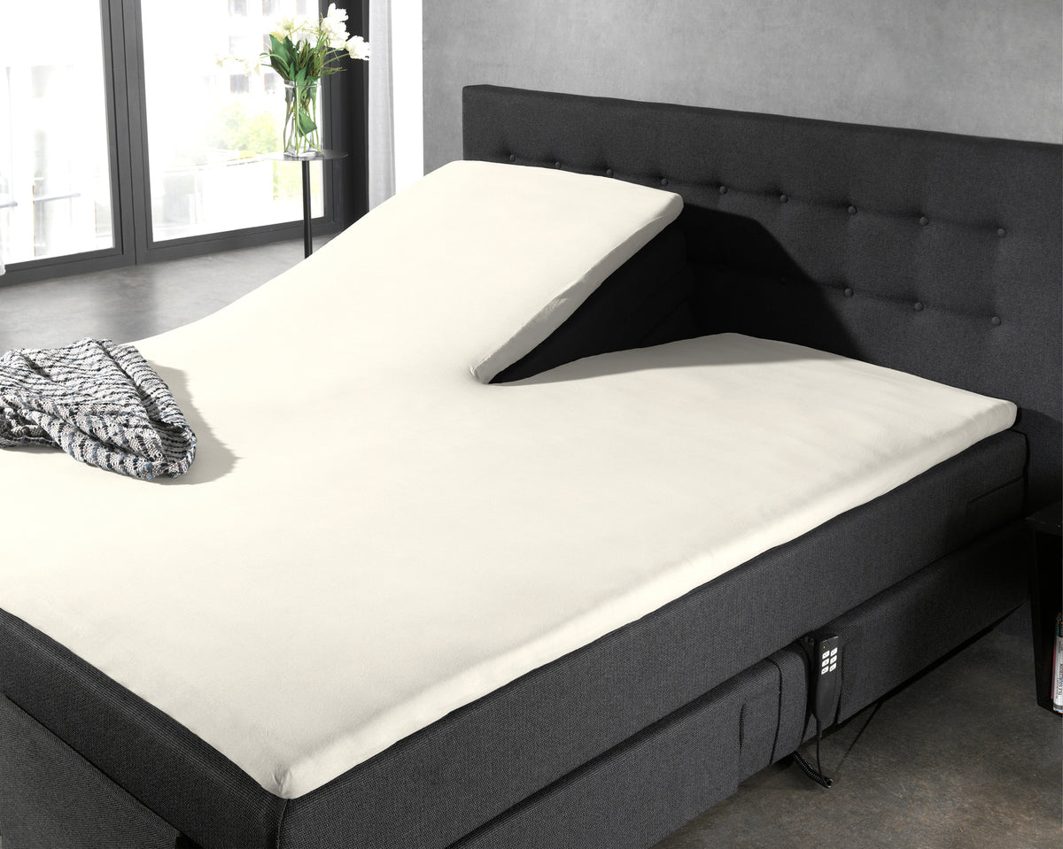 Crèmekleurig hoeslaken op een split-topper op een donkergrijs boxspringbed met een omhoog gezet hoofdeinde