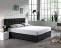 Wit hoeslaken op een boxspring met donker gecapitonneerd hoofdbord in een slaapkamer met witte bakstenen muur