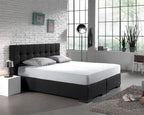 Wit hoeslaken op een boxspring met donker gecapitonneerd hoofdbord in een slaapkamer met witte bakstenen muur