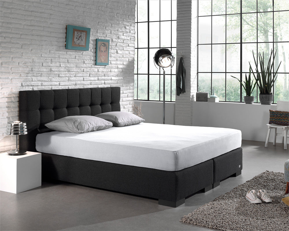Wit hoeslaken op een boxspring met donker gecapitonneerd hoofdbord in een slaapkamer met witte bakstenen muur