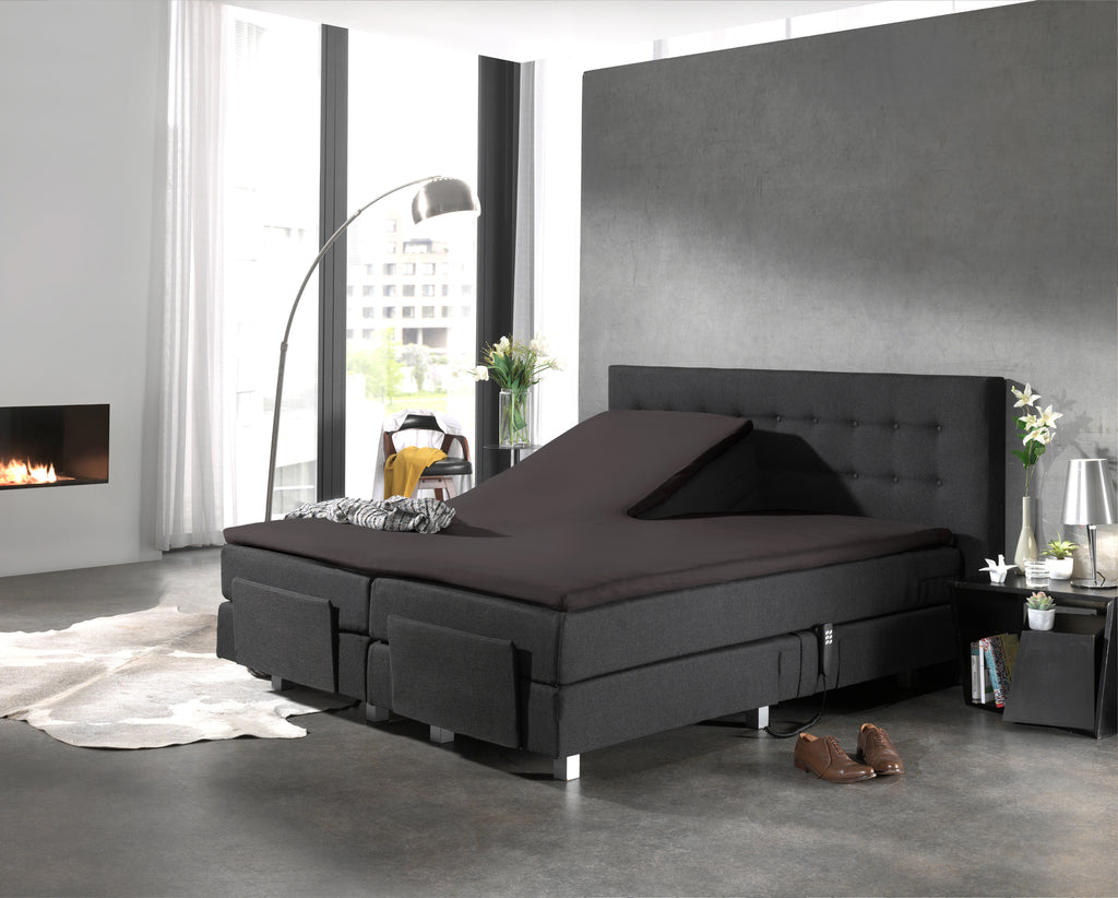 Boxspring met gesplitste topper en donker hoeslaken in een moderne slaapkamer met grijze muur