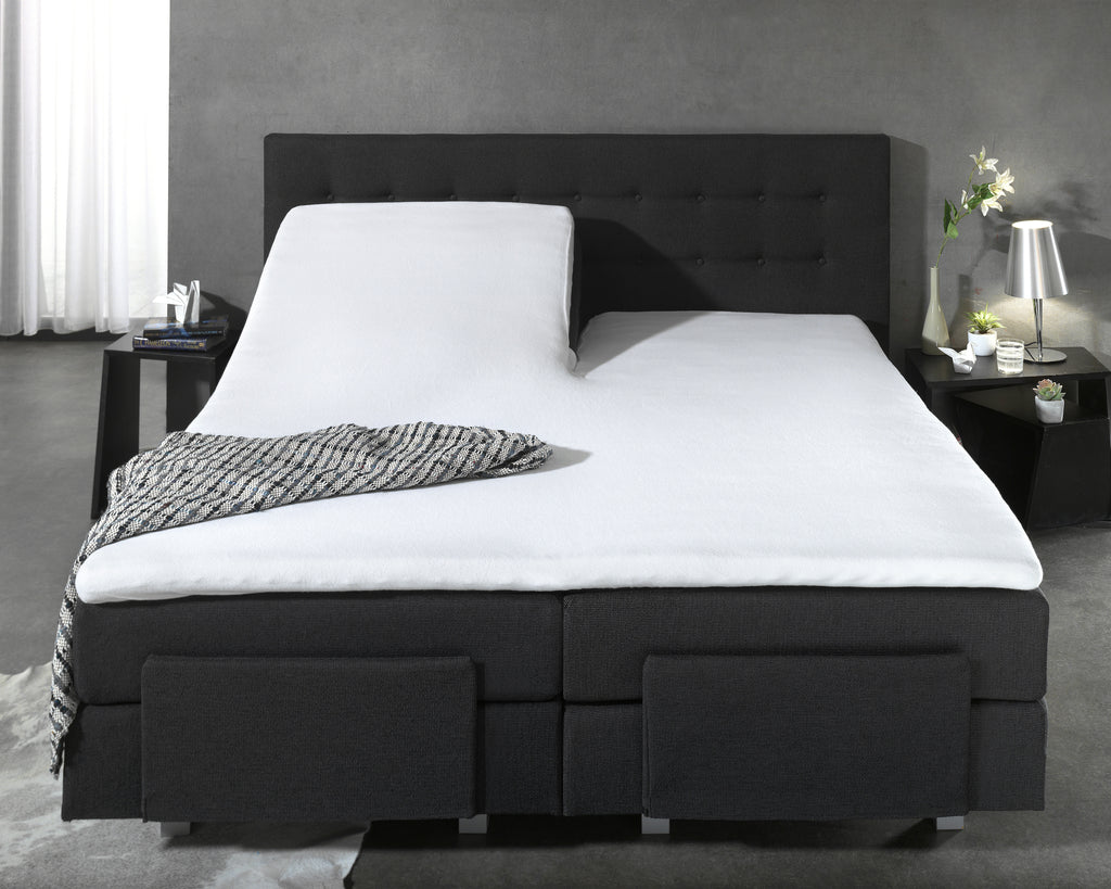 Wit molton hoeslaken op een gesplitste topper op een zwarte boxspring met een gestreepte plaid