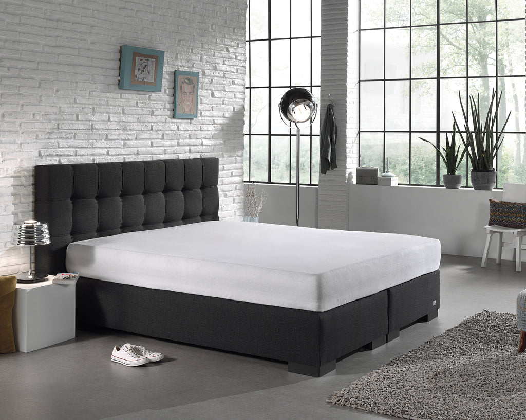 Wit molton hoeslaken op een matras met donkergrijs boxspringbed en gecapitonneerd hoofdbord in een slaapkamer