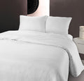 Wit dekbedovertrek met subtiele hotelstrepen en twee kussens op een bed tegen een donkere wand