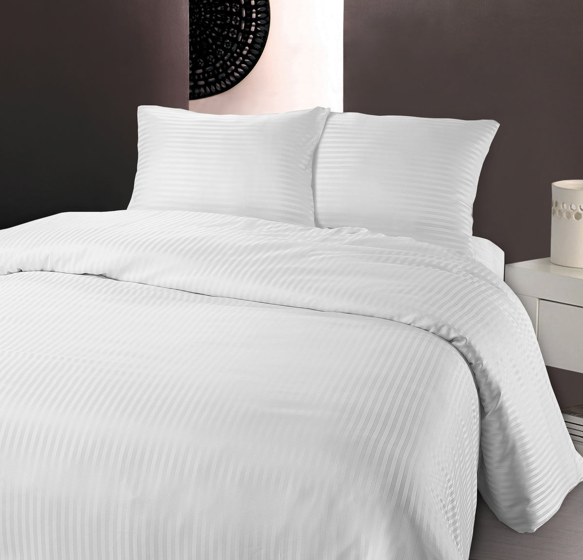 Wit dekbedovertrek met subtiele hotelstrepen en twee kussens op een bed tegen een donkere wand