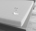 Wit waterdicht hoeslaken op een matras met een omgevallen glas waarvan het water op het laken blijft liggen