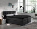 Zwart jersey hoeslaken op een donkere boxspring met grijze kussens in een lichte slaapkamer met witte baksteenmuur