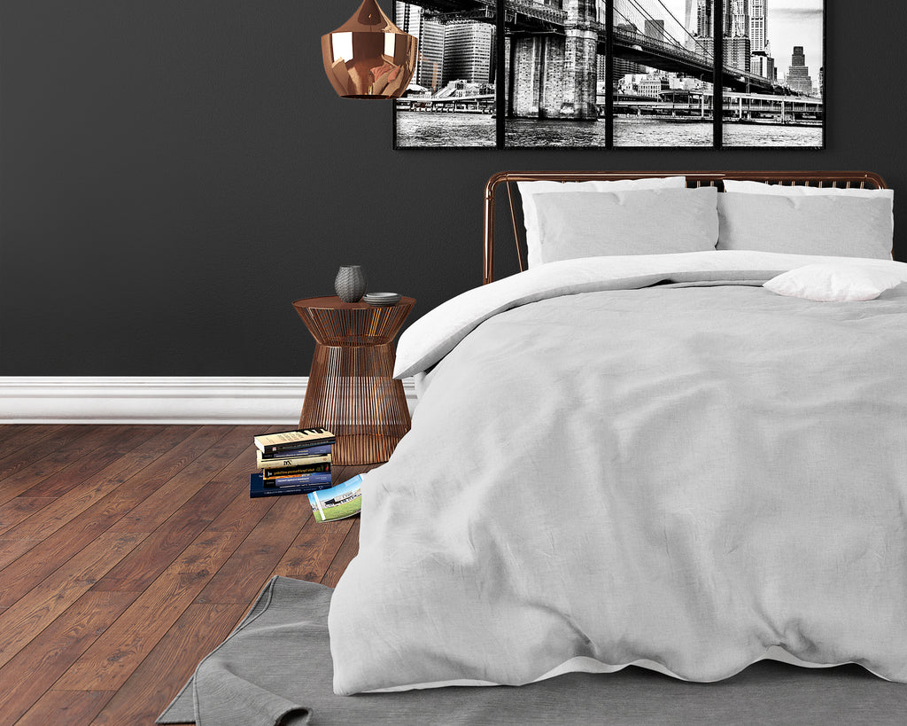 Opgemaakt bed met lichtgrijs dekbedovertrek en kussens voor een donkere muur met koperen hanglamp
