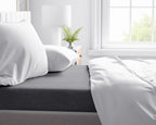 Antracietgrijs laken op een bed met witte kussens en een wit dekbedovertrek naast een raam