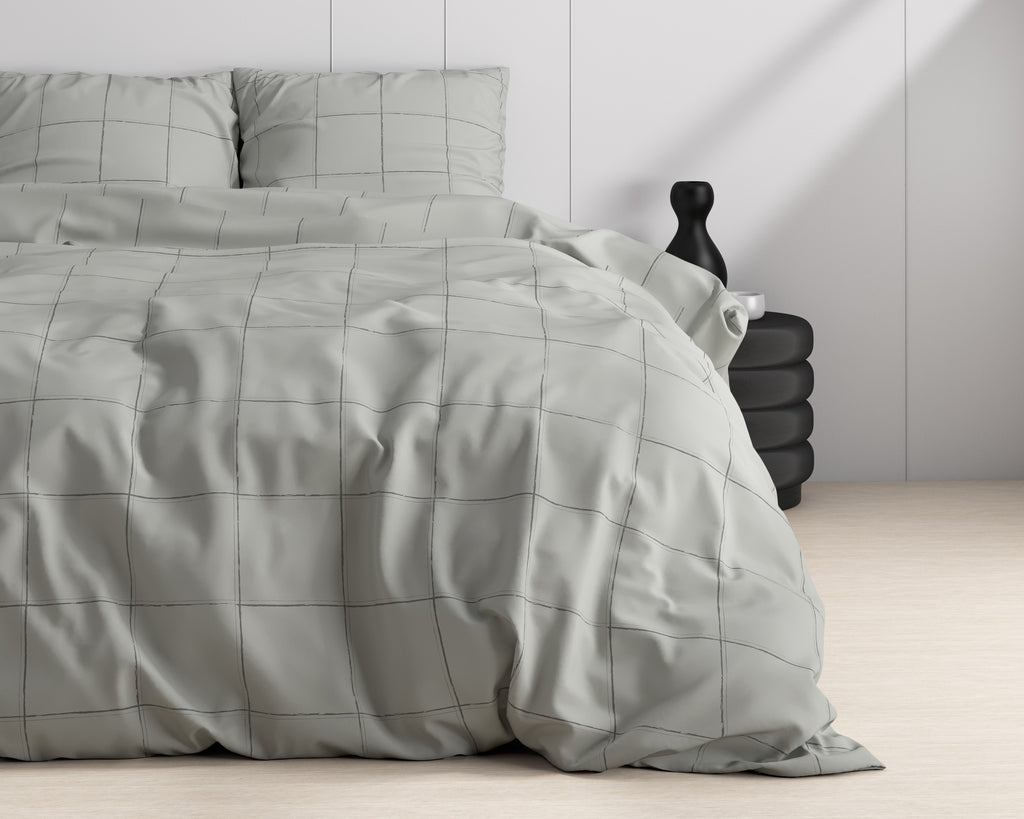 Grijs dekbedovertrek met ruitprint en bijpassende kussenslopen op een bed, naast een zwart bijzettafeltje