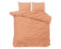 Pastel oranje dekbedovertrek met twee kussenslopen op een bed, effen met subtiel geëmbosseerd structuurpatroon