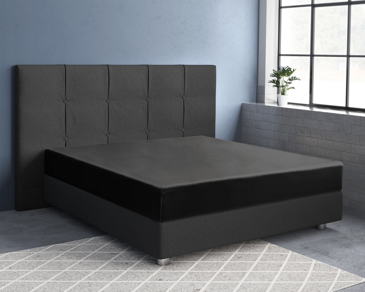 Zwart satijnen hoeslaken op een matras met grijs gestoffeerd hoofdbord in een slaapkamer met blauwe muur