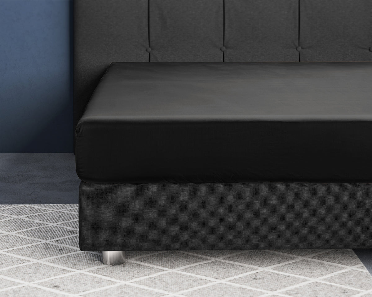 Zwart satijnen hoeslaken over een matras op een grijze boxspring met gecapitonneerd hoofdbord