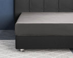 Grijs satijnen hoeslaken over een matras op een donkergrijs gestoffeerd boxspringbed met bijpassend hoofdbord