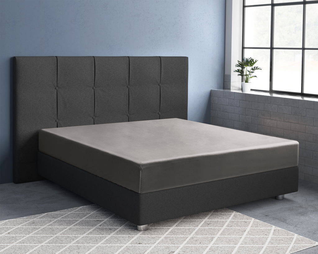 Grijs satijnen hoeslaken op een bed met donker gestoffeerd hoofdbord in een kamer met blauwe muur