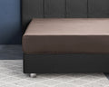 Taupe hoeslaken van satijn strak om een matras op een donkergrijs boxspringbed met gestoffeerd hoofdbord