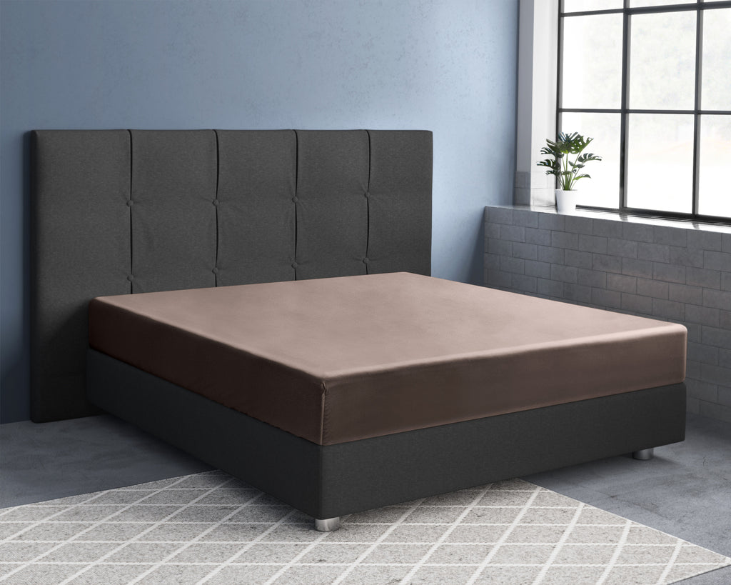 Taupe satijnen hoeslaken op een bed met donkergrijs gestoffeerd hoofdbord en boxspringbasis in een slaapkamer met blauwe muur