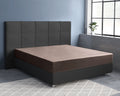 Taupe satijnen hoeslaken om een matras op een donkergrijs gestoffeerd bed met hoofdbord in een blauwgrijze slaapkamer