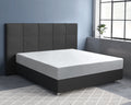 Wit hoeslaken over matras op donkergrijs boxspringbed met gecapitonneerd hoofdbord in kamer met blauwe muur