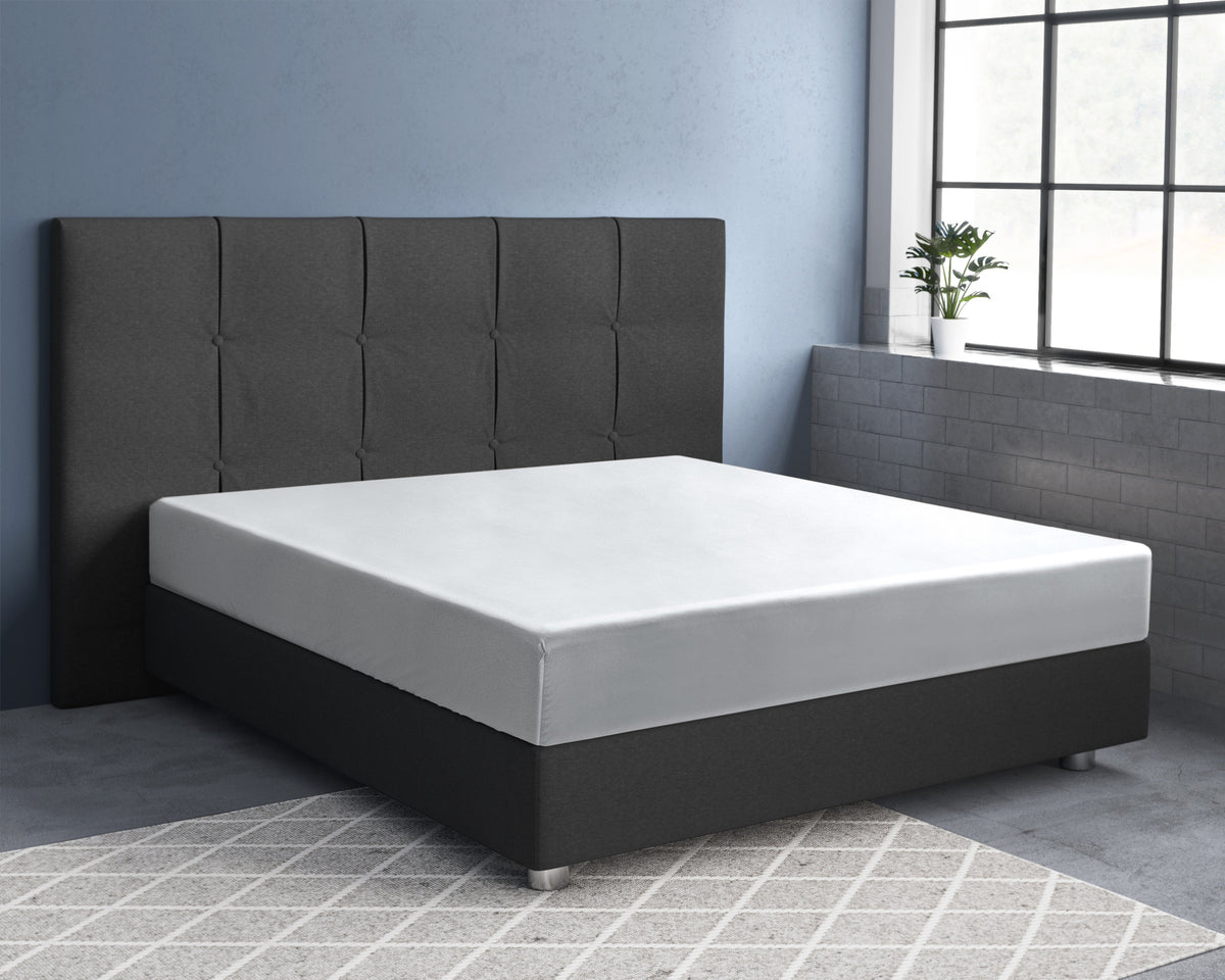 Wit hoeslaken over matras op donkergrijs boxspringbed met gecapitonneerd hoofdbord in kamer met blauwe muur