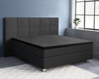 Zwarte boxspring met donker gestoffeerd hoofdbord en zwarte topper in een kamer met blauwe muur en groot raam
