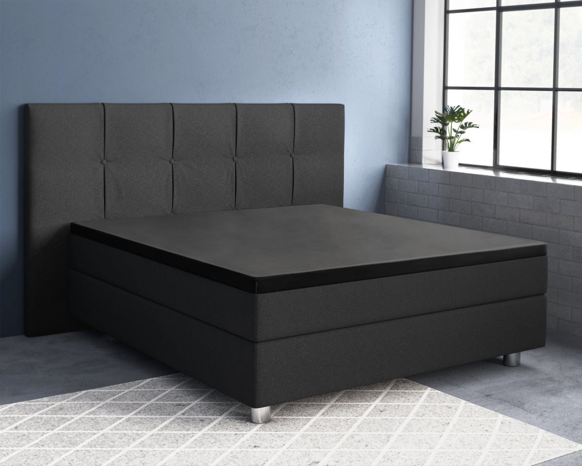 Boxspring met donkergrijs hoofdbord en zwart topperhoeslaken in een slaapkamer met blauwe muur en groot raam
