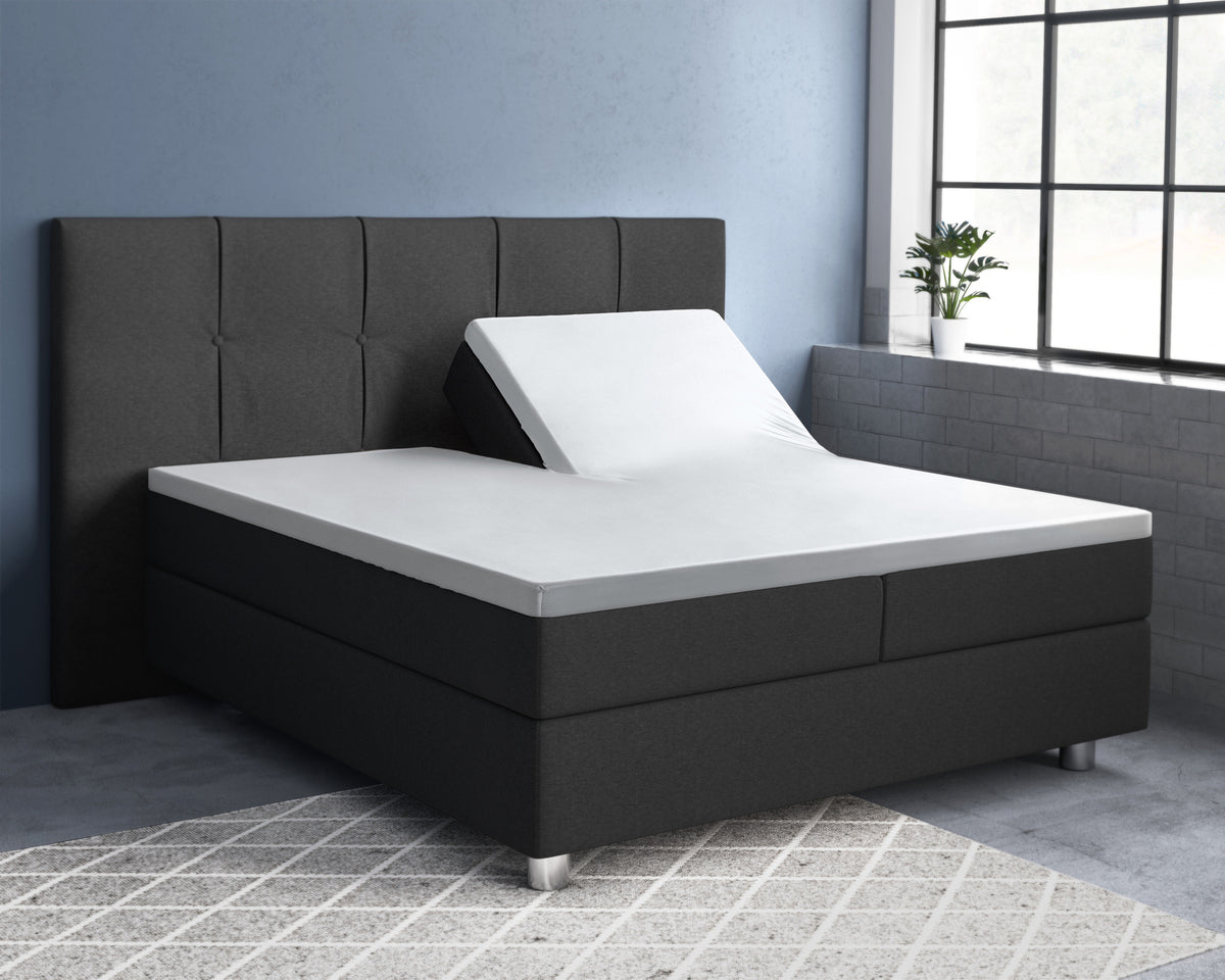 Wit splittopper hoeslaken op een antracietkleurig boxspringbed met gestoffeerd hoofdbord, één helft omhoog gesteld