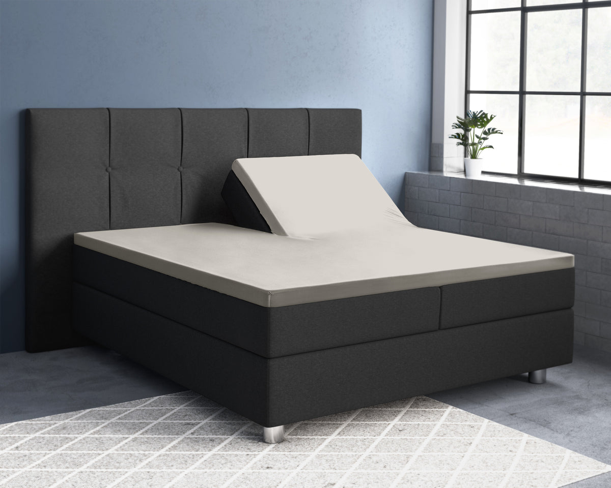 Crèmekleurig splittopper hoeslaken op een antracietgrijs boxspringbed met één hoofdeinde omhoog gezet