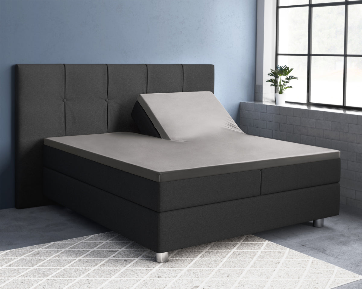 Grijs splittopper hoeslaken op een antracietkleurig boxspringbed, met de rechterhelft van het hoofdeinde omhoog gezet