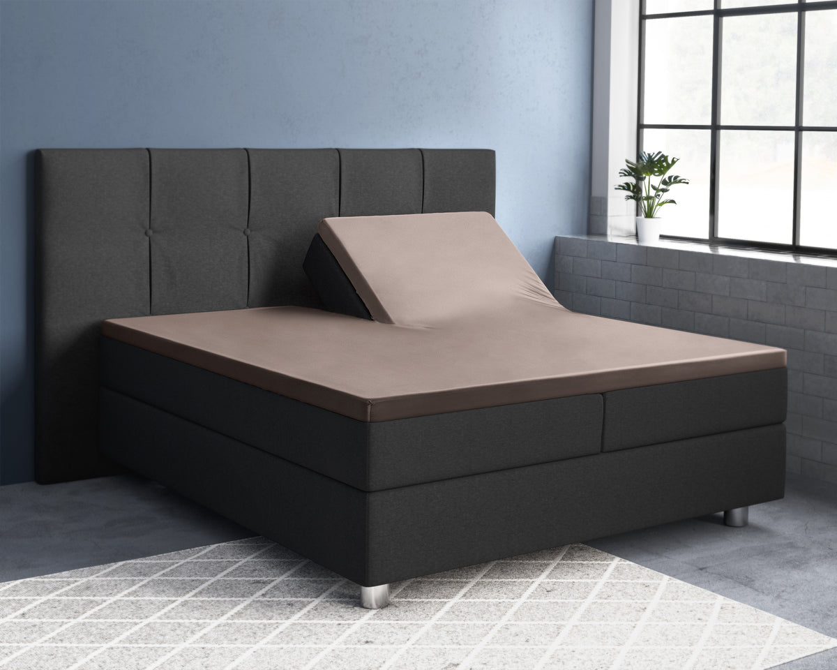 Taupe splittopper hoeslaken op een donkergrijs boxspringbed, met de ene helft omhoog gesteld