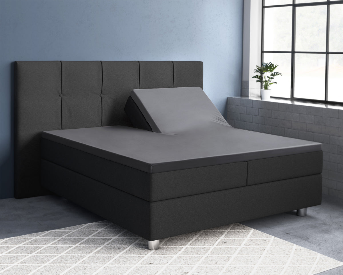 Antracietgrijs hoeslaken op een splittopper met opgeklapte rechterzijde, op een boxspring met donker hoofdbord
