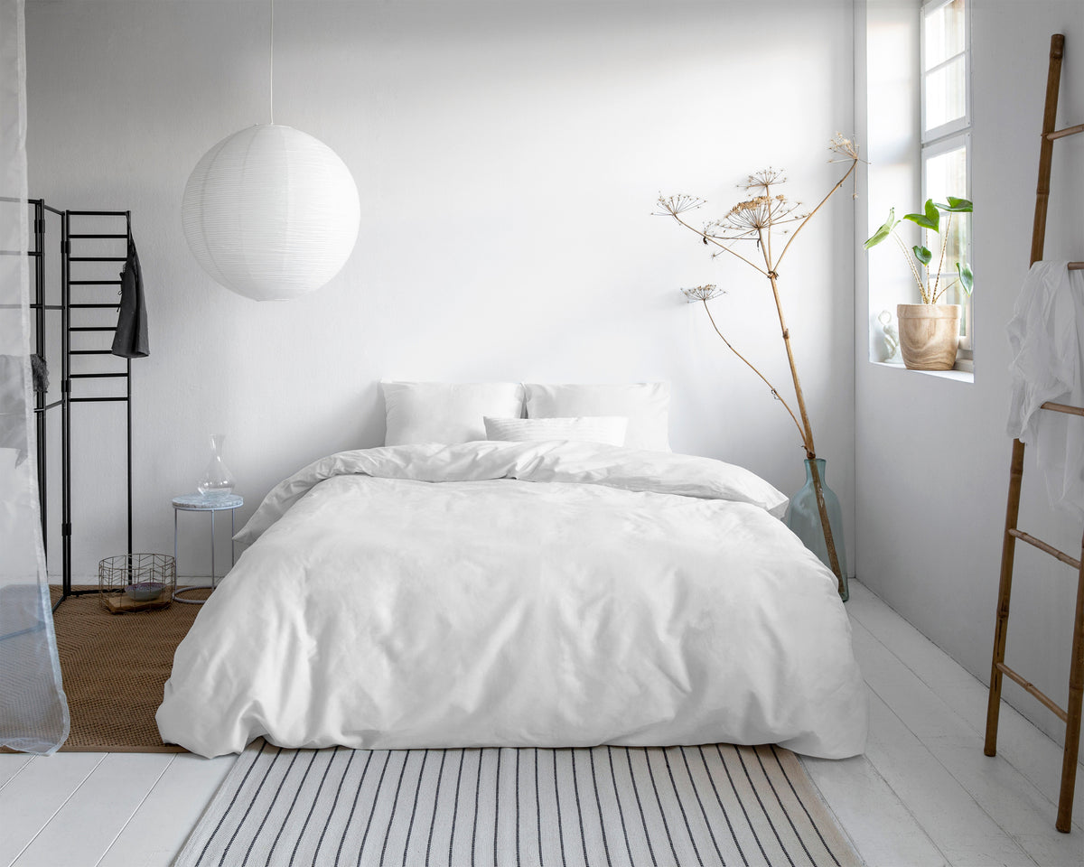 Wit dekbedovertrek met kussens op een bed in een lichte slaapkamer met ronde papieren hanglamp