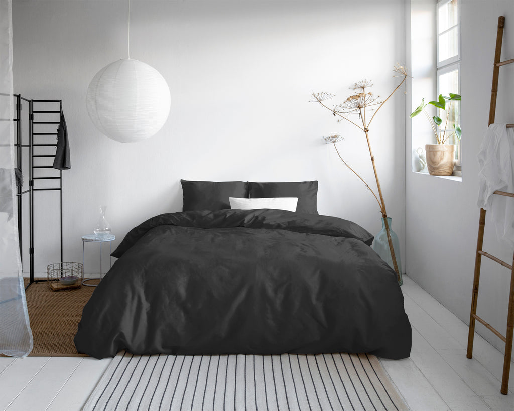 Zwart satijnen dekbedovertrek op een bed in een lichte slaapkamer met witte hanglamp en gestreept vloerkleed