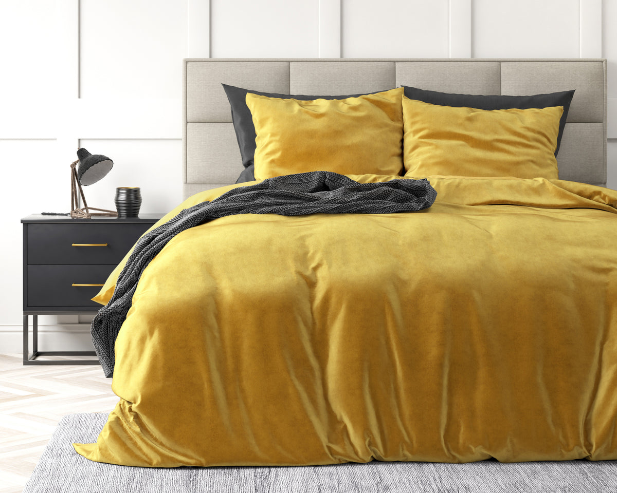 Goudkleurig velvet dekbedovertrek met kussenslopen op een bed met grijs hoofdbord en antracietkleurige plaid