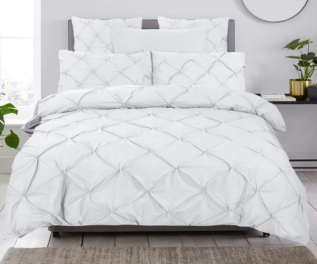 Bed opgemaakt met wit pintuck dekbedovertrek en bijpassende kussens in een lichte slaapkamer
