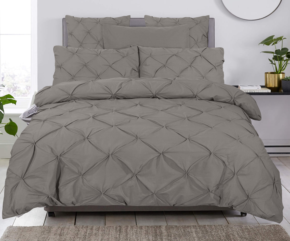 Opgemaakt bed met taupe dekbedovertrek en kussens met pintuck-dessin in een lichte slaapkamer