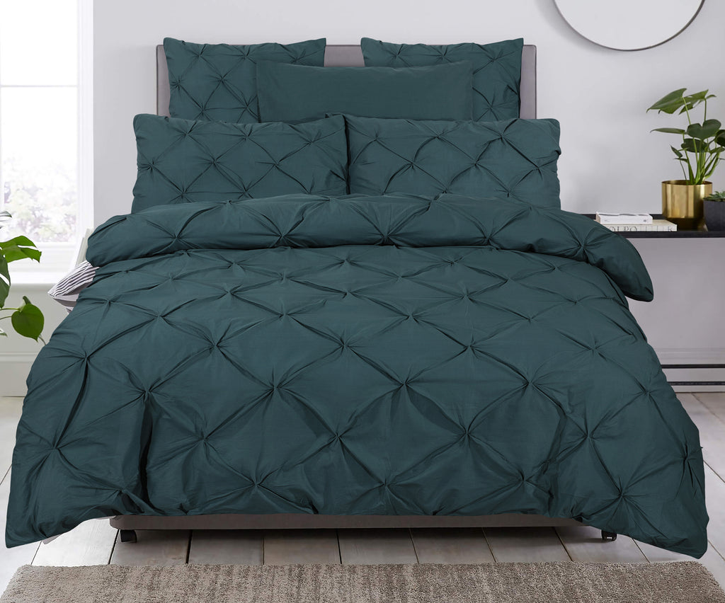 Bed met donkergroen pintuck dekbedovertrek en bijpassende kussens in een lichte slaapkamer