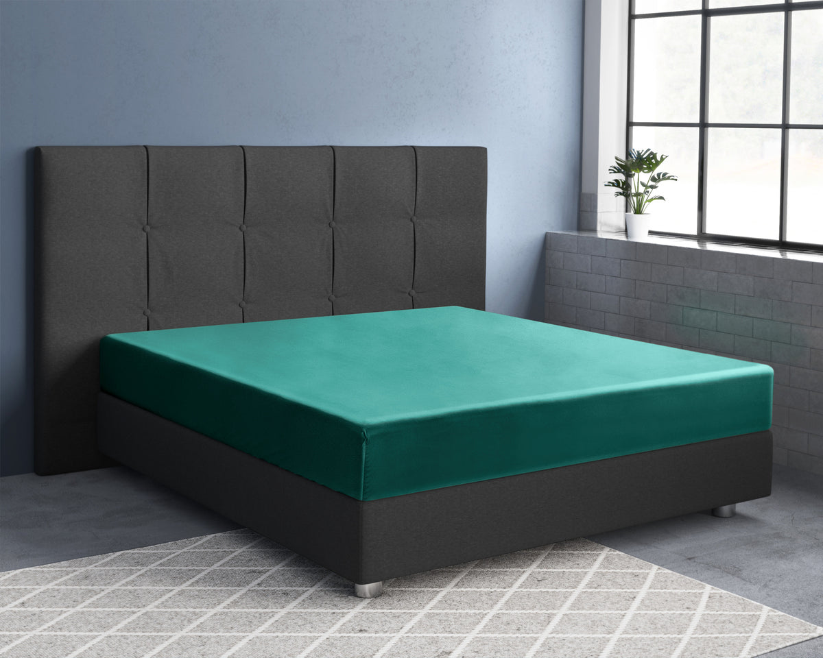 Donkergroen satijnen hoeslaken op een bed met grijs gestoffeerd hoofdbord in een slaapkamer met groot raam