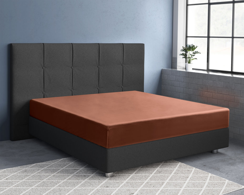 Bruin hoeslaken van katoensatijn op een bed met donkergrijs gestoffeerd hoofdbord in een slaapkamer met raam