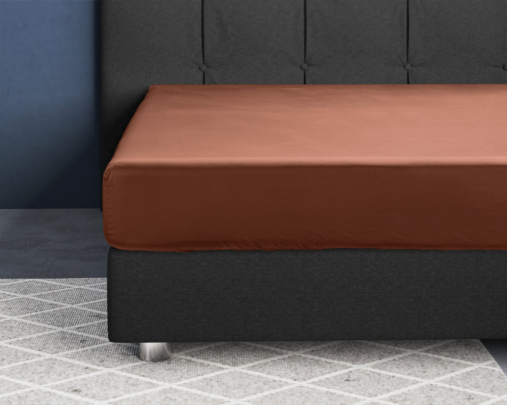 Bruin hoeslaken van katoensatijn strak over een matras op een donkergrijs boxspringbed