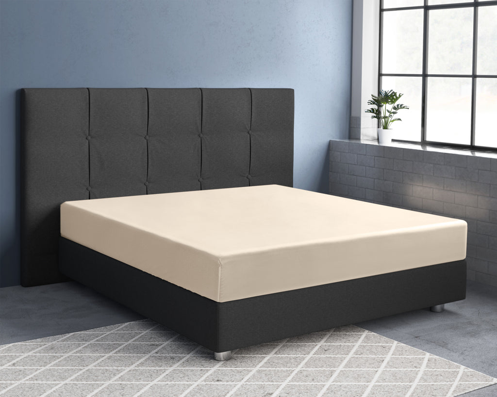 Zandkleurig hoeslaken van katoensatijn op een matras met donkergrijs boxspringbed en gecapitonneerd hoofdbord