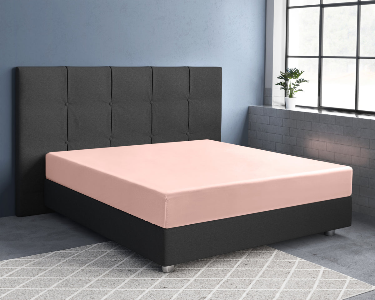 Roze hoeslaken van katoensatijn om een matras op een donkergrijs boxspringbed met gecapitonneerd hoofdbord