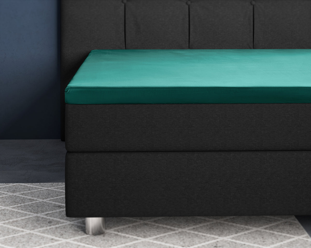 Donkergroen satijnen hoeslaken om een topper op een zwarte boxspring met gestoffeerd hoofdbord