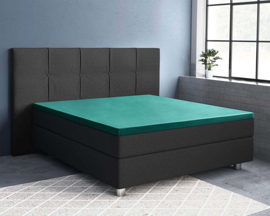 Donkergroen satijnen topperhoeslaken op een antraciet boxspringbed met gestoffeerd hoofdbord in een slaapkamer