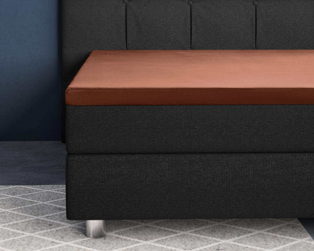 Bruin satijnen topper hoeslaken strak om een topper op een donkergrijs boxspringbed
