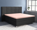 Roze satijnen hoeslaken op een oplegmatras van een zwart bed met gestoffeerd hoofdbord in een blauwgrijze slaapkamer