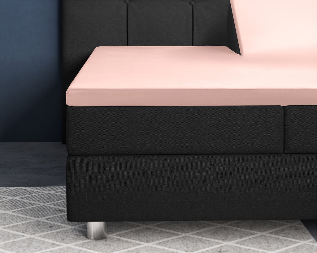 Roze satijnen splittopper hoeslaken op een zwarte boxspring met verstelbaar hoofdeinde