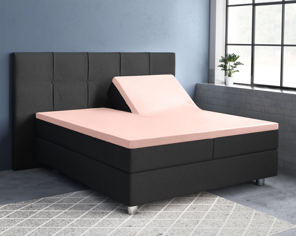 Roze satijnen splittopper hoeslaken op een boxspring met donkergrijs hoofdbord, één hoofdeinde omhoog gezet